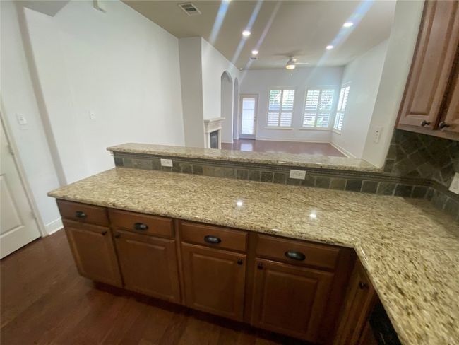 Kitchen with ceiling fan, dark wood-style floors, light stone counters, arched walkways, and decorative backsplash | Image 11