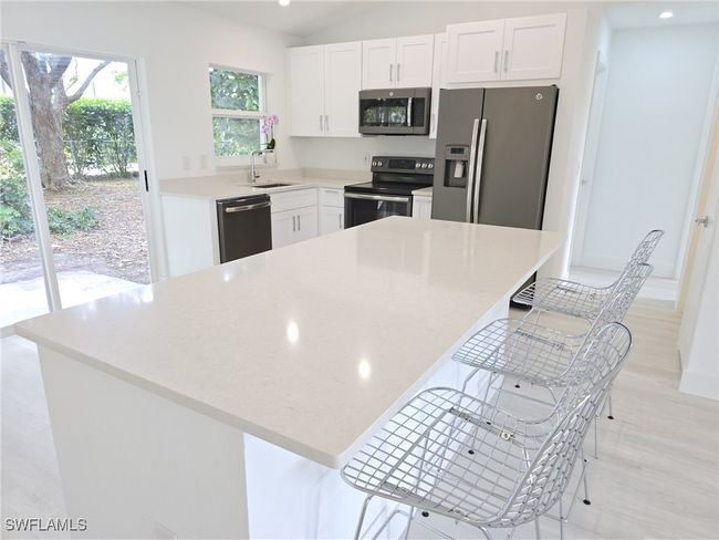 Kitchen with stainless steel appliances, a sink, white cabinets, a kitchen bar, and recessed lighting | Image 5
