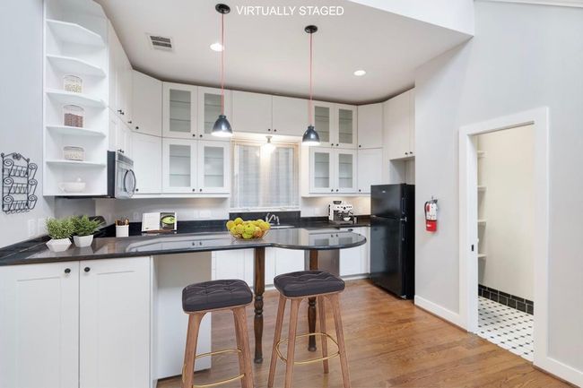 Kitchen featuring freestanding refrigerator, open shelves, dark countertops, a kitchen breakfast bar, and white cabinetry | Image 28