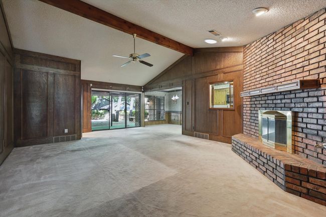 Unfurnished living room featuring vaulted ceiling with beams, wooden walls, ceiling fan, a brick fireplace, and visible vents | Image 20