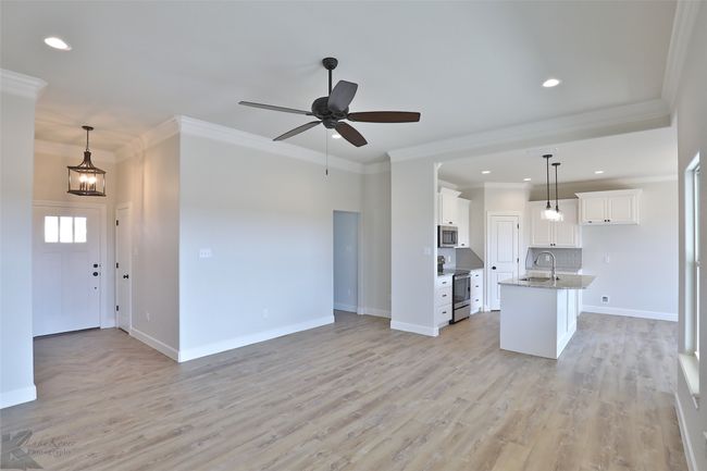 Kitchen featuring appliances with stainless steel finishes, open floor plan, white cabinetry, hanging light fixtures, and crown molding | Image 6