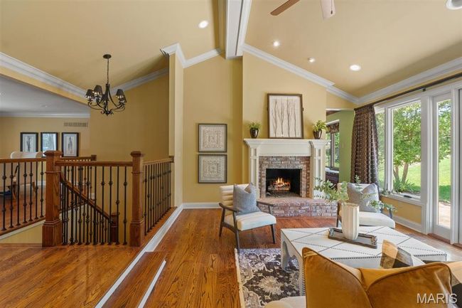 Living area featuring wood finished floors, a fireplace, a chandelier, ceiling fan, and ornamental molding | Image 6