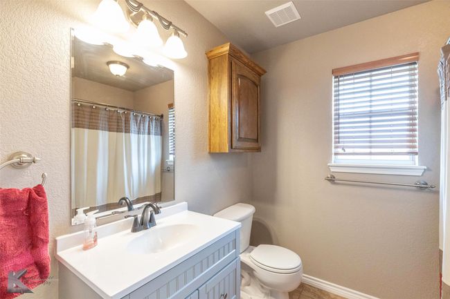 Bathroom featuring toilet, vanity, a textured wall, and a shower with shower curtain | Image 24