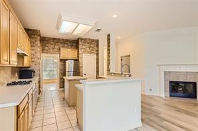 Kitchen with a center island with sink, light countertops, open floor plan, under cabinet range hood, and a fireplace | Image 5