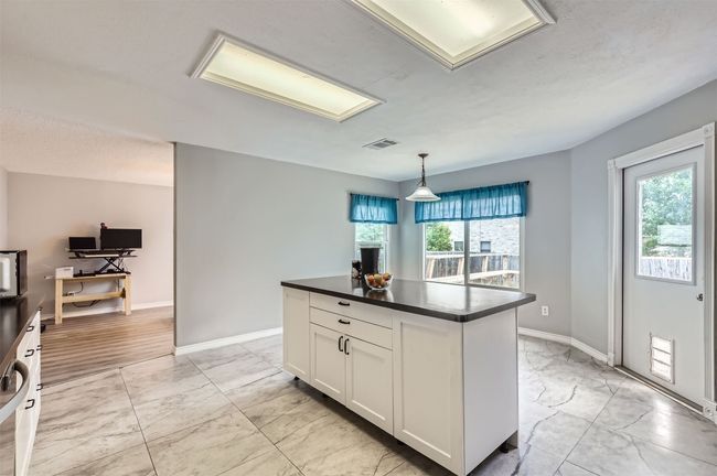 Kitchen with light marble finish floors, dark countertops, white cabinetry, a kitchen island, and baseboards | Image 12