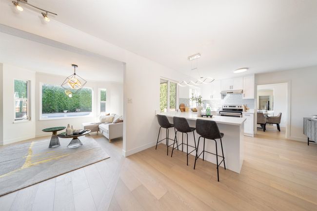 Kitchen featuring a peninsula, a kitchen bar, under cabinet range hood, white cabinetry, and stainless steel electric stove | Image 13