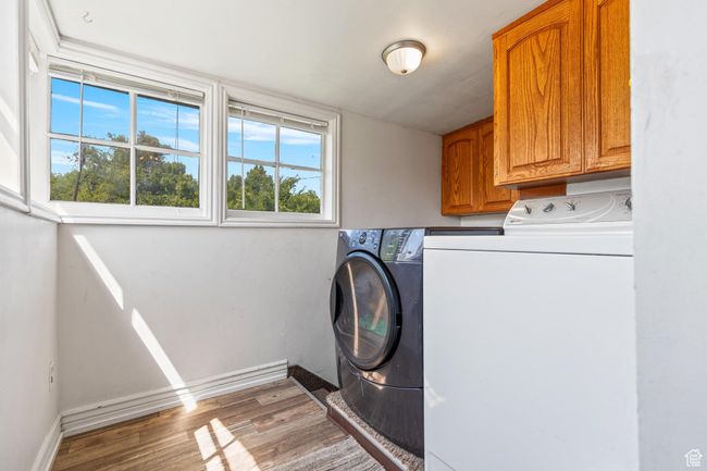 Laundry area featuring cabinet space, washing machine and clothes dryer, wood finished floors, and baseboards | Image 11