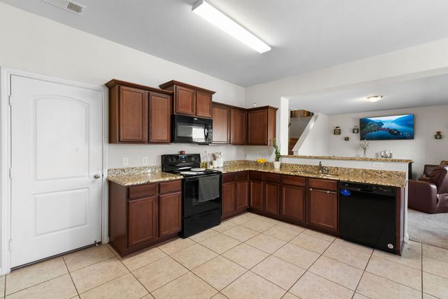 Kitchen featuring a peninsula, a sink, light tile patterned flooring, open floor plan, and black appliances | Image 10