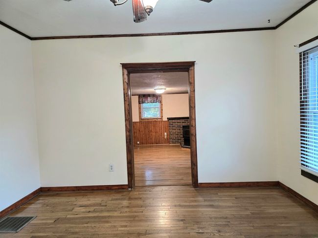 Unfurnished room with ceiling fan, crown molding, a brick fireplace, and wood-type flooring | Image 5
