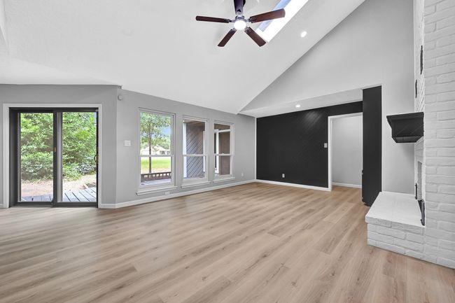 Spacious living room featuring soaring vaulted ceilings, a dramatic black accent wall, and a skylight that floods the space with natural light. Large windows and sliding glass doors offer serene views and seamless access to the backyard deck—perfect for entertaining or relaxing at home | Image 7