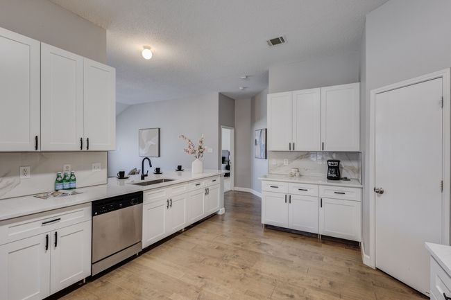 Kitchen with stainless steel dishwasher, a sink, light countertops, white cabinets, and vaulted ceiling | Image 9