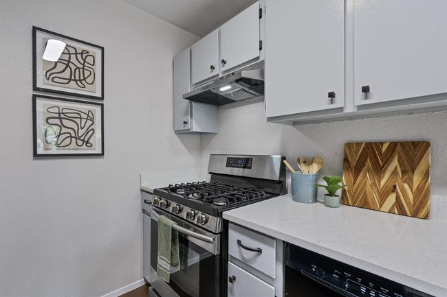 Kitchen featuring stainless steel gas range oven, under cabinet range hood, light stone counters, and white cabinetry | Image 10
