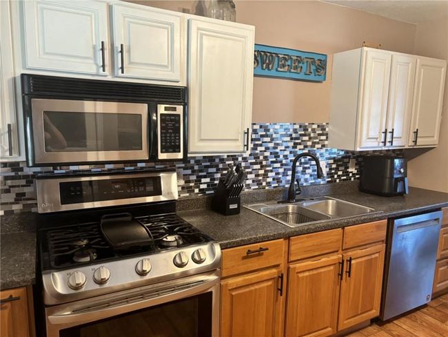 Kitchen with appliances with stainless steel finishes, a sink, tasteful backsplash, and dark countertops | Image 8