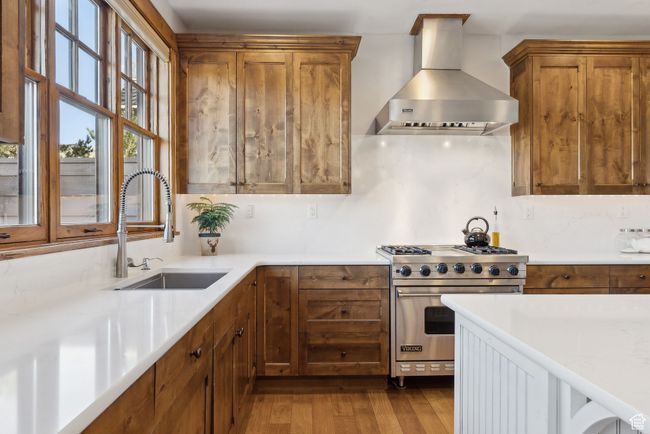 Kitchen with brown cabinets, wood finished floors, a sink, premium range, and wall chimney exhaust hood | Image 11
