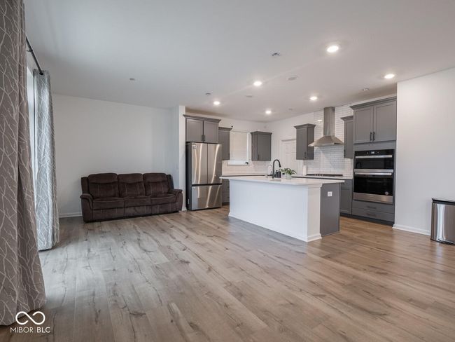 kitchen with wall chimney exhaust hood, open floor plan, light wood-style floors, stainless steel appliances, and gray cabinets | Image 15