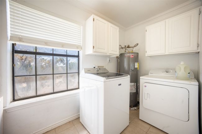 Clothes washing area with water heater, washer and clothes dryer, light tile patterned floors, and cabinet space | Image 15