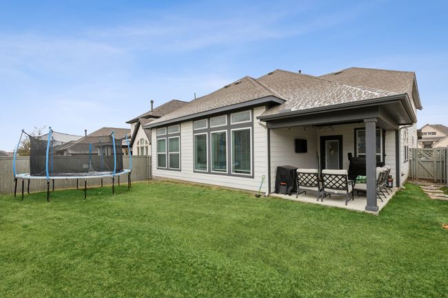 Rear view of house with a patio area, a fenced backyard, a trampoline, and a yard | Image 28