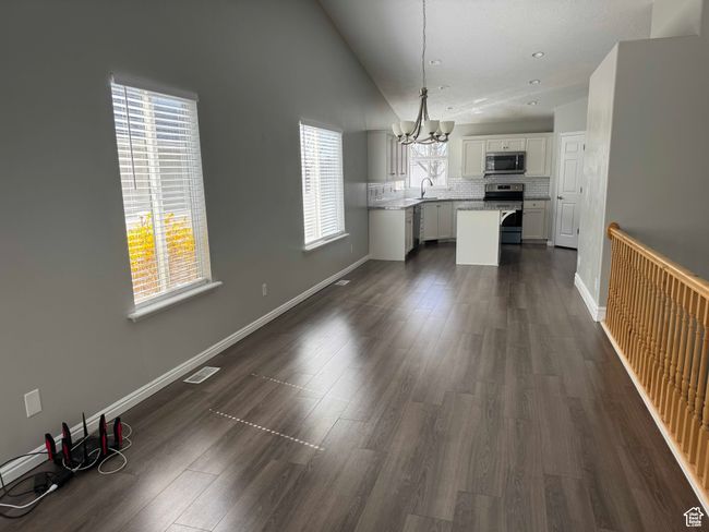 Unfurnished dining area with a chandelier, a sink, dark wood finished floors, vaulted ceiling, and baseboards | Image 4
