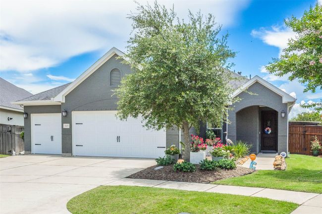 The garage doors, crafted with fine detail, complement the home’s exterior, enhancing its overall curb appeal. Lush landscaping frames the entrance, with manicured lawns and vibrant flower beds adding a touch of color and life. | Image 10