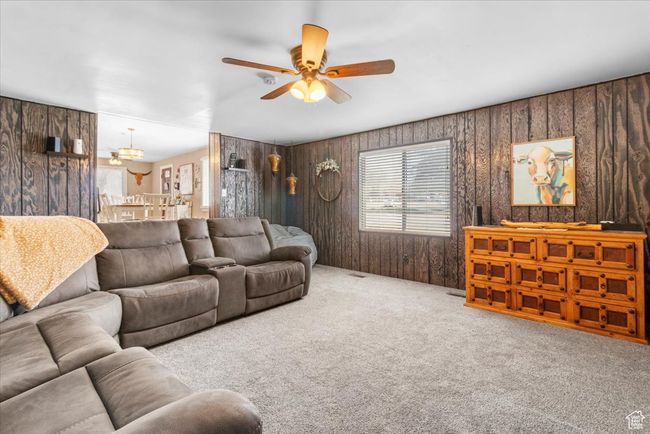 Carpeted living room with ceiling fan with notable chandelier and wooden walls | Image 29