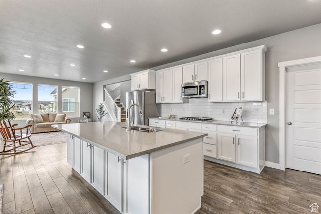 Kitchen featuring a sink, dark wood-type flooring, a center island with sink, appliances with stainless steel finishes, and white cabinetry | Image 16
