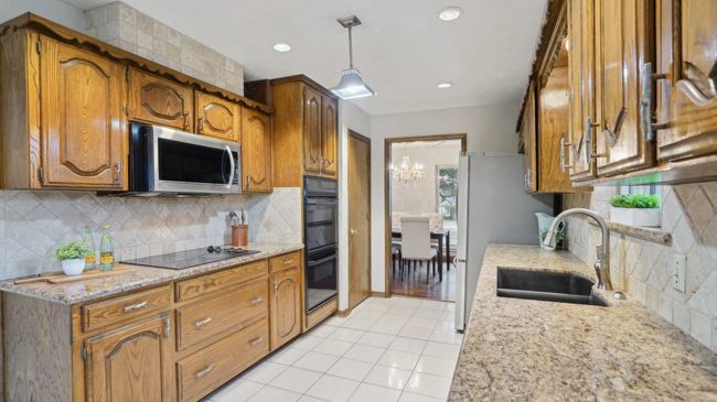 Kitchen featuring brown cabinets, a sink, tasteful backsplash, black appliances, and light tile patterned flooring | Image 13