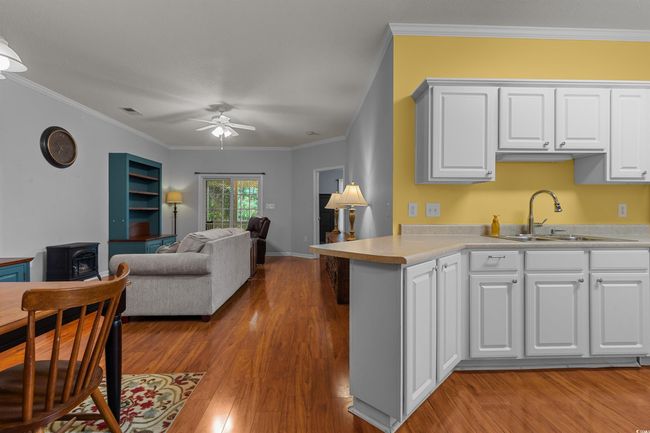 Kitchen with a sink, a wood stove, light wood-style floors, a ceiling fan, and crown molding | Image 11