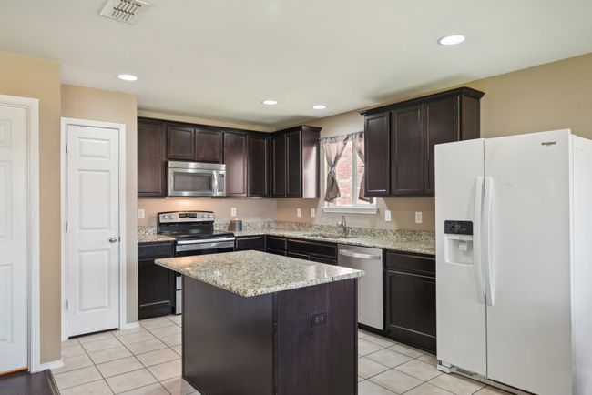 Kitchen with light tile patterned floors, a sink, visible vents, dark brown cabinets, and appliances with stainless steel finishes | Image 12