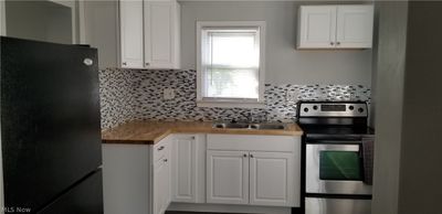 Kitchen featuring backsplash, black fridge, butcher block countertops, stainless steel range with electric cooktop, and sink | Image 2