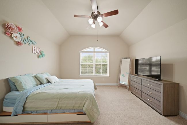 This bedroom features a vaulted ceiling, large window for natural light, and neutral carpeting and a ceiling fan. | Image 28