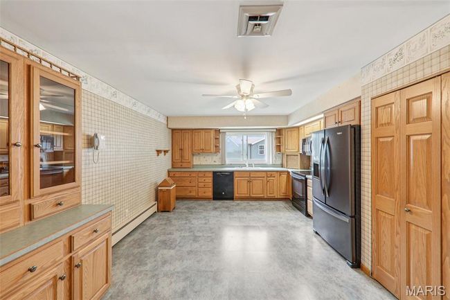 Kitchen featuring black appliances, a baseboard heating unit, a ceiling fan, wallpapered walls, and light countertops | Image 12