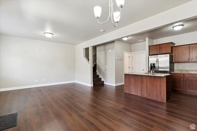 Kitchen with stainless steel fridge with ice dispenser, dark wood-style floors, a chandelier, a center island with sink, and baseboards | Image 6