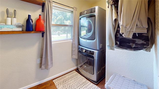Laundry area with a textured wall, stacked washer and clothes dryer, and wood finished floors | Image 17