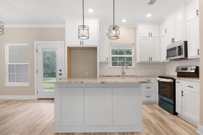 This modern kitchen features white cabinetry, a spacious marble island, and stainless steel appliances. It has a bright, open layout with natural light streaming through large windows and a glass door leading to the backyard. Perfect for cooking and entertaining. | Image 9