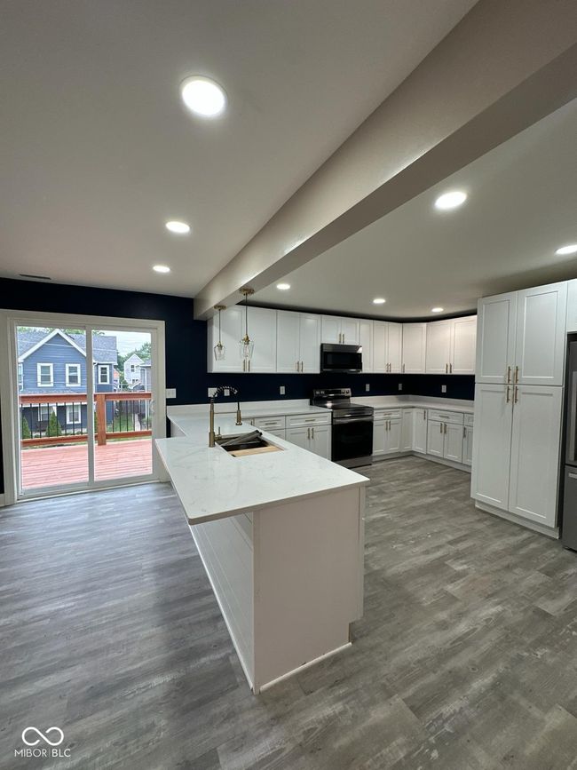 Unit 2 - kitchen featuring electric stove, black microwave, a peninsula, white cabinets, and wood finished floors | Image 16