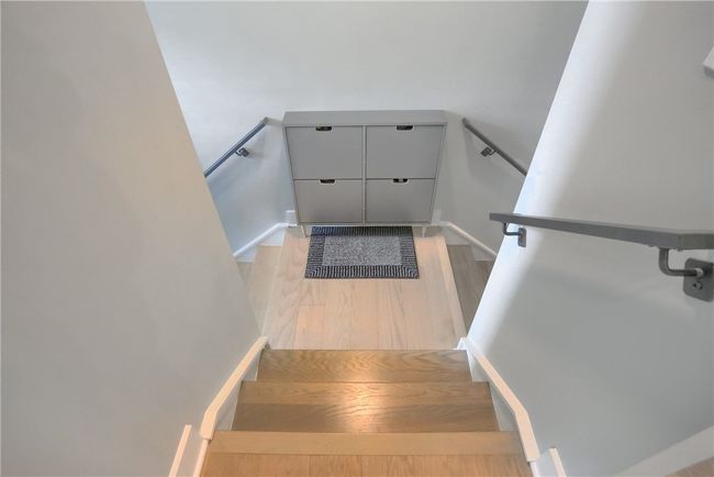 The entryway sets a clean and modern tone with light hardwood flooring, neutral walls, and sleek metal railings leading up from a smartly organized drop zone. | Image 5