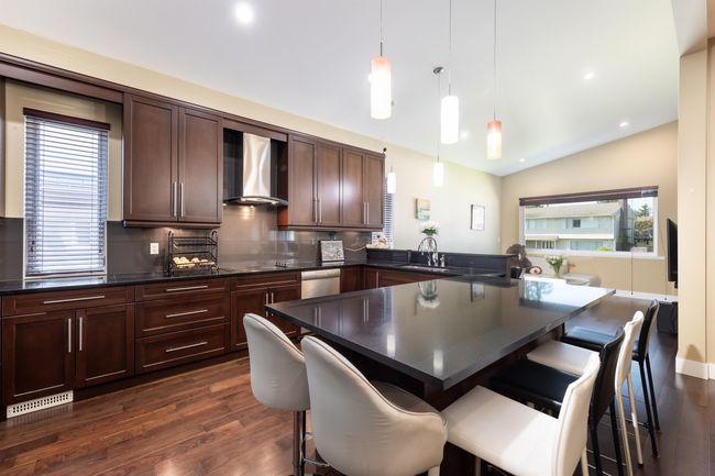 Kitchen featuring wall chimney exhaust hood, dark wood-style floors, dark countertops, a peninsula, and backsplash | Image 12