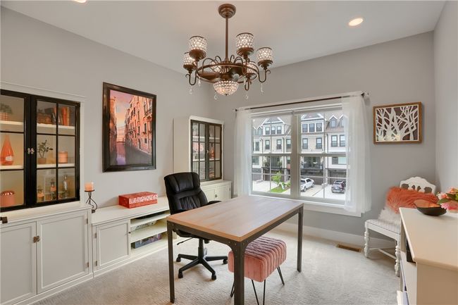 This inviting den with French door access offers a perfect work-from-home setup, featuring custom built-ins, elegant display cabinets, and a statement chandelier—all framed by a large window overlooking the charming townhome community. | Image 16