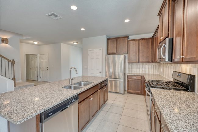Kitchen featuring visible vents, a sink, backsplash, appliances with stainless steel finishes, and light stone countertops | Image 14