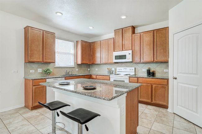Kitchen with white appliances, a breakfast bar area, light stone counters, brown cabinetry, and recessed lighting | Image 18