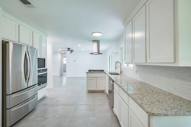 Kitchen featuring appliances with stainless steel finishes, island range hood, backsplash, ceiling fan, and white cabinetry | Image 14