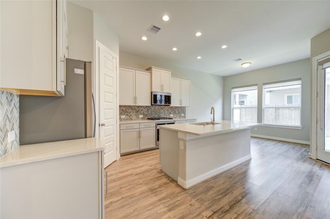 Modern kitchen with an open layout, featuring sleek cabinetry, a large island with a sink, and stainless steel appliances. The space is bright with ample natural light. | Image 8