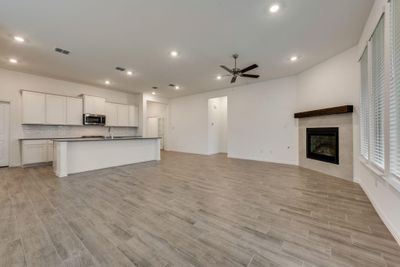 Unfurnished living room featuring a tiled fireplace, ceiling fan, sink, and light hardwood / wood-style floors | Image 3