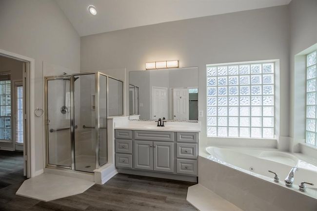 Master bathroom features a modern design with a spacious glass-enclosed shower, a large corner tub, and ample natural light from frosted glass block windows. It includes a wide his and her vanity with dual sinks and contemporary fixtures, set against stylish flooring. | Image 30