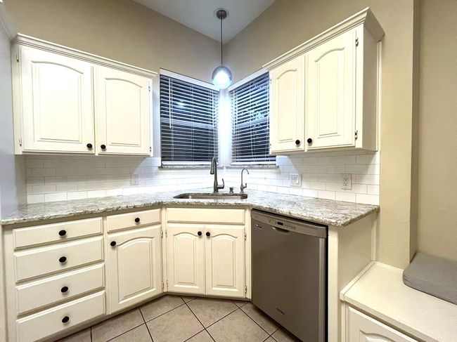 Kitchen with dishwasher, decorative backsplash, light tile patterned floors, hanging light fixtures, and light stone counters | Image 7