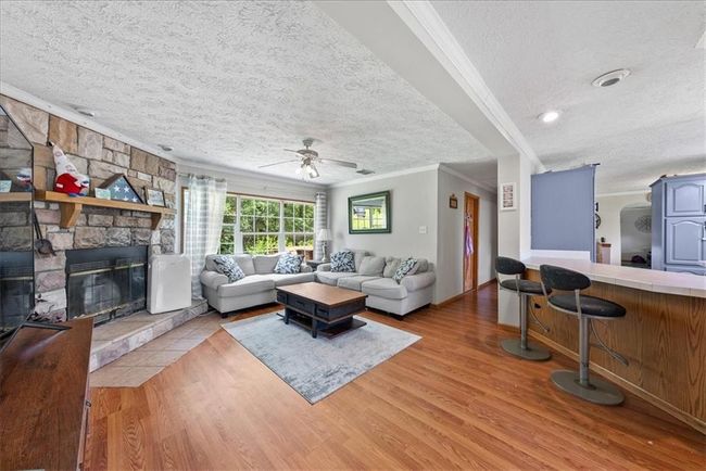 Living room featuring a ceiling fan, crown molding, a textured ceiling, and wood finished floors | Image 7