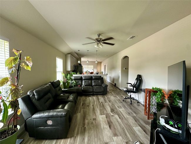 Living area featuring light wood finished floors, a ceiling fan, and arched walkways | Image 10