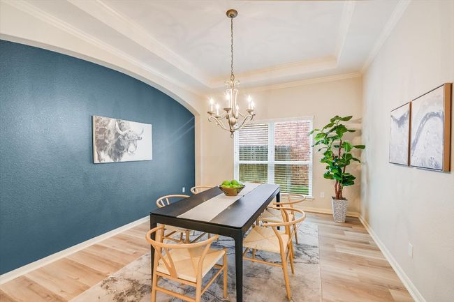 Dining area featuring a chandelier, light wood finished floors, a raised ceiling, crown molding, and arched walkways | Image 14
