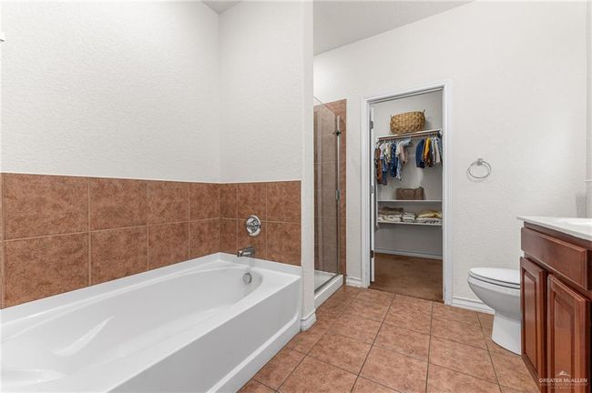 Full bathroom featuring a garden tub, vanity, a textured wall, a stall shower, and a walk in closet | Image 8