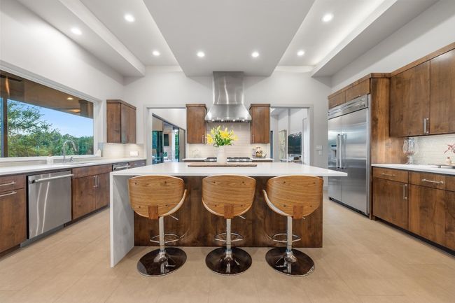 Kitchen with tasteful backsplash, wall chimney range hood, appliances with stainless steel finishes, light countertops, and a breakfast bar area | Image 10